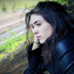 Liebeskummer Überwinden: 5 Unverzichtbare Tipps für Deinen Weg zurück zur Liebe Eine nachdenkliche Frau blickt traurig zu Boden, symbolisiert durch ihre bedrückte Haltung, während sie über den Schmerz von Liebeskummer und Trennung nachdenkt.