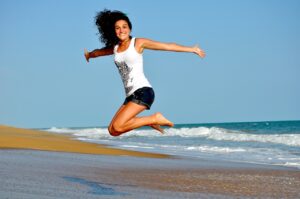 Fremdgänger-Quote: Was die Körbchen- und die Schuhgröße über die Treue aussagen soll Eine glückliche Frau springt am Strand in die Höhe, symbolisiert Freude und Selbstbewusstsein, während sie die Diskussion über den Zusammenhang zwischen Brustgröße und Treue anregt.